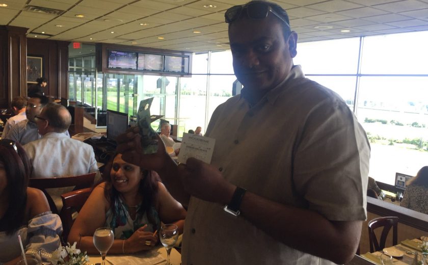 Woodbine Races, man smiling inside in the brown dining area, wearing dark sunglasses on head, holding money